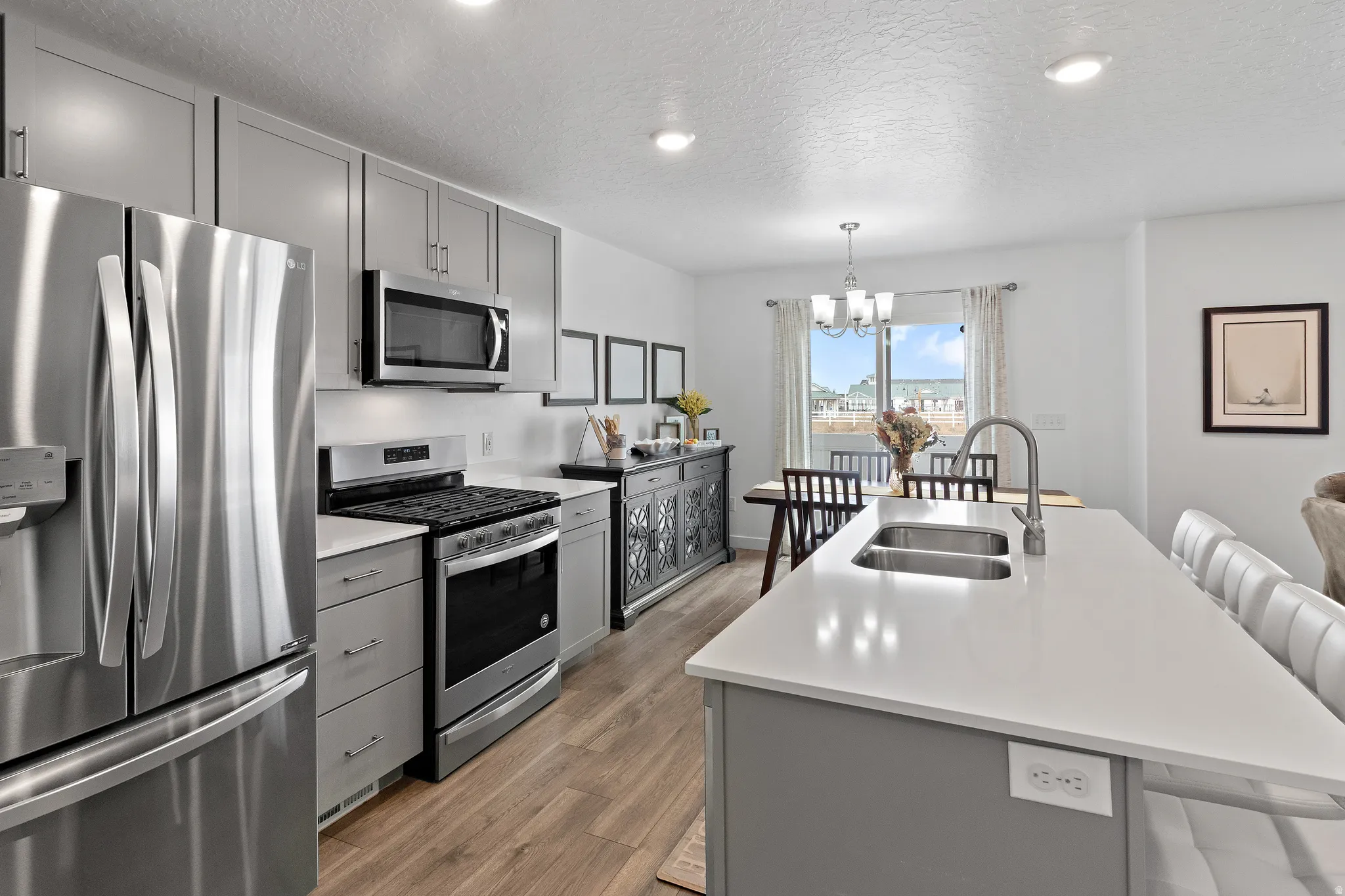 Kitchen featuring gray cabinetry, stainless steel appliances, a kitchen island with sink, a kitchen breakfast bar, and a textured ceiling