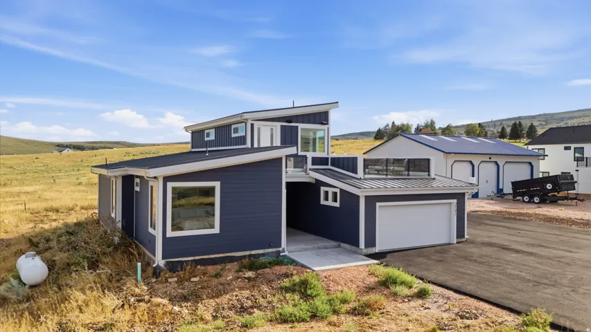 Contemporary exterior featuring blue siding, white trim, a single-car garage, and a separate detached two-bay garage