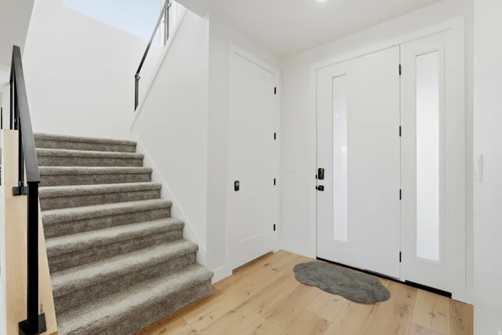 Hardwood-style flooring throughout, white walls, carpeted staircase, black metal stair railing, and a modern entry door with side lites