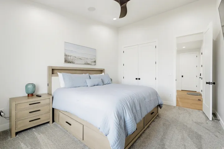 Recessed lighting, wood-finish bed frame with built-in storage, light-toned carpet, built-in closet with double doors, and wood-finish flooring in the entryway