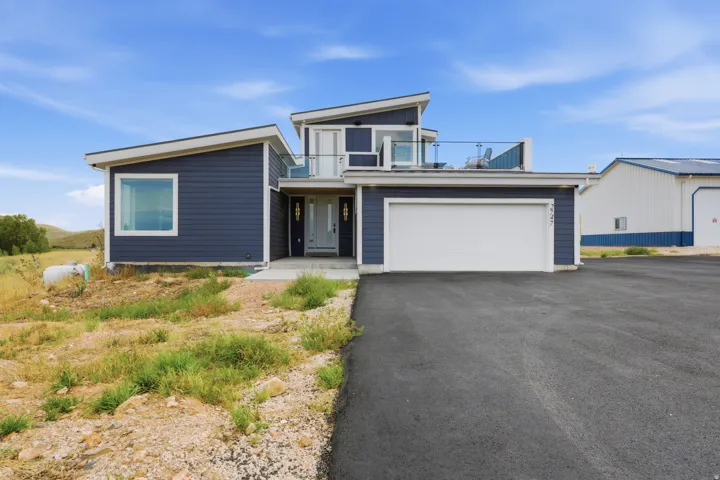 Contemporary-style residence with dark blue siding, a two-car garage, and an upper-level balcony featuring a glass railing