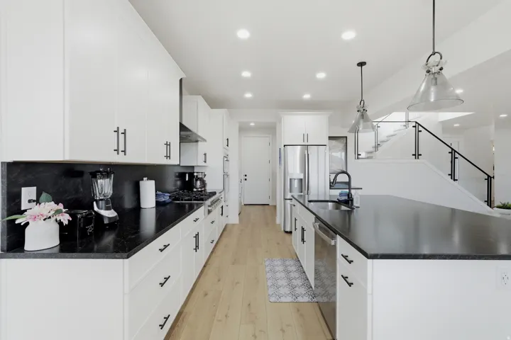 Contemporary kitchen with white cabinetry, dark countertops, wood-finish flooring, stainless steel appliances, and a central island with an undermount sink