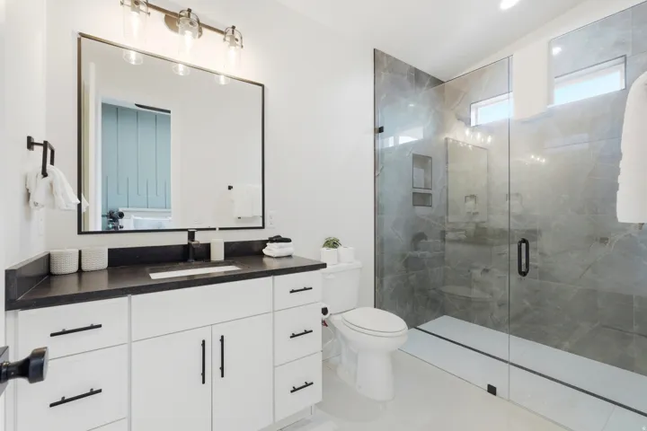 White vanity with dark countertop, large framed mirror, and chrome-finish light fixture