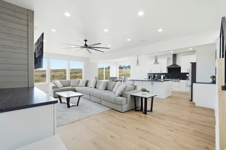 Expansive open-concept living area featuring wood-finish flooring, numerous windows, recessed lighting, and a modern ceiling fan