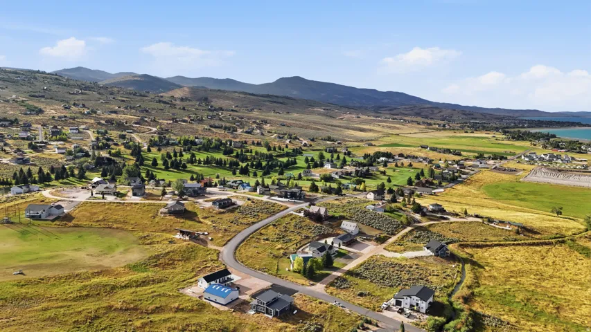 Expansive aerial perspective showcasing a residential community, surrounding mountain ranges, a golf course, and a body of water