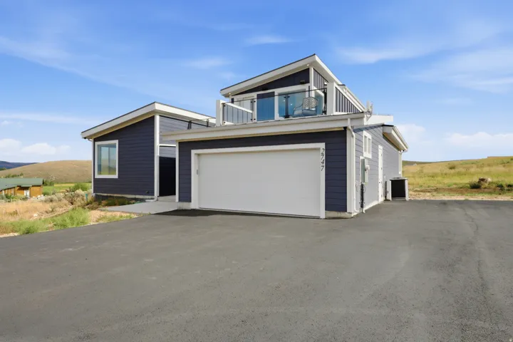 Contemporary exterior with dark siding, attached garage, and a second-story balcony with glass railing