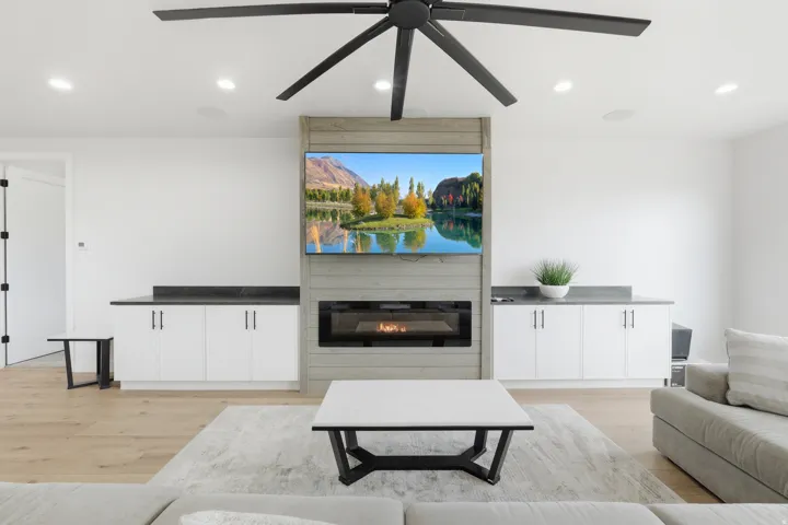 Wood-finish flooring, built-in cabinetry with dark countertops, linear electric fireplace, recessed lighting, and a large ceiling fan
