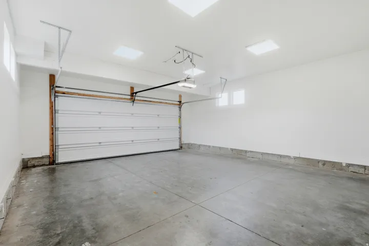 Spacious garage featuring a concrete floor, white panel garage door, multiple windows, and recessed lighting fixtures