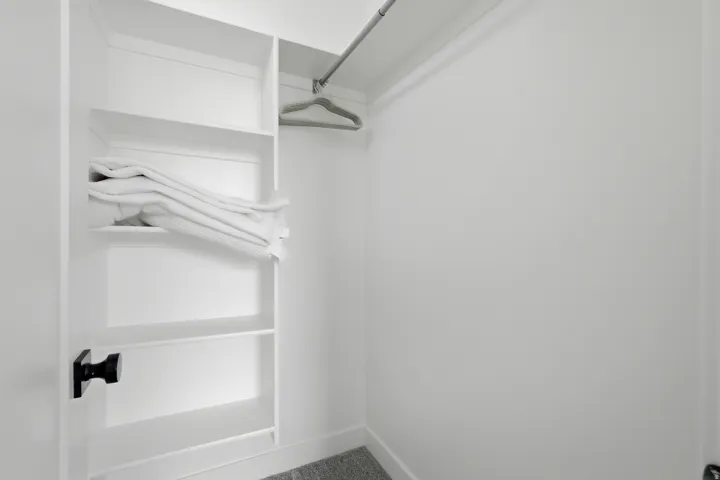 Built-in shelving, white walls, and a metal hanging rod provide versatile storage