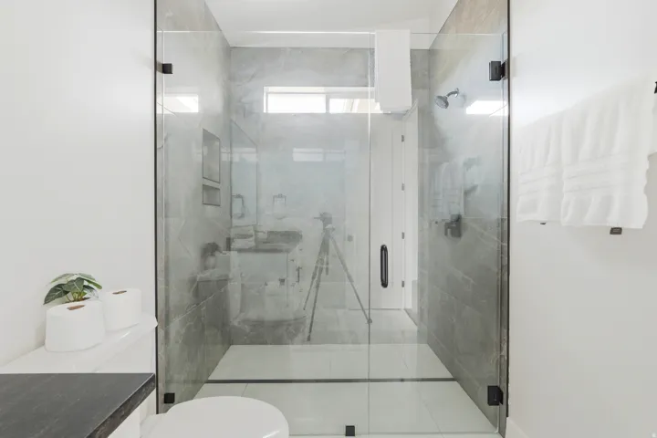 Glass-enclosed shower with gray tiled walls and a white tiled floor