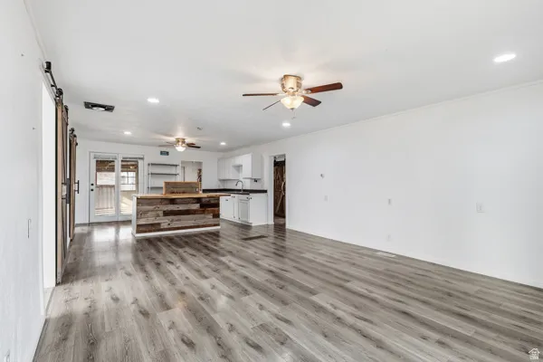 Unfurnished living room with a barn door, light wood-style flooring, recessed lighting, and a ceiling fan