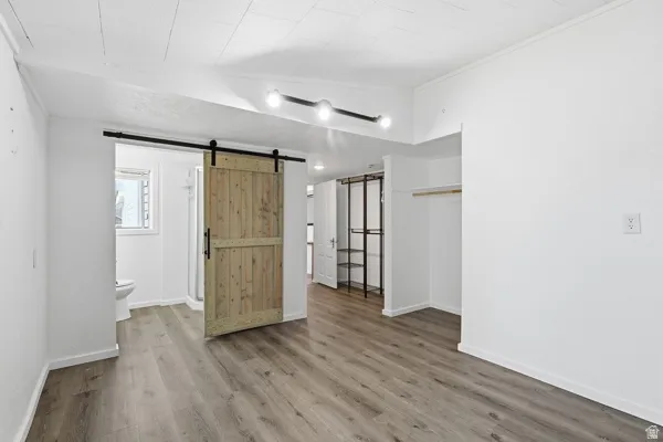 Unfurnished bedroom featuring a barn door, wood finished floors, crown molding, and ensuite bath