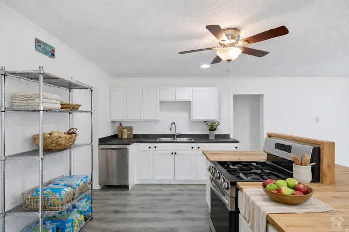 Kitchen with stainless steel appliances, white cabinetry, ceiling fan, light wood finished floors, and a textured ceiling