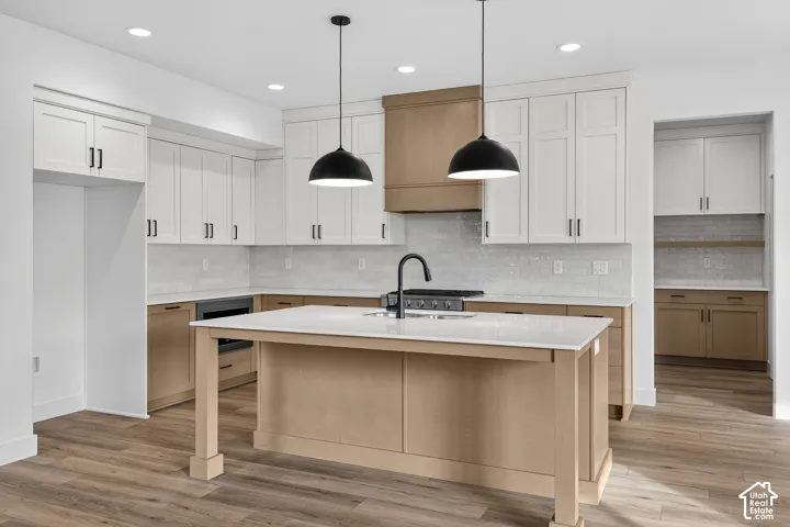 Kitchen with light wood-style floors, two tone cabinetry, an island with sink, decorative light fixtures, and a kitchen bar