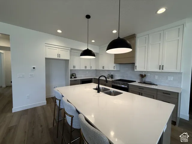 Recessed lighting, wood-finish flooring, full height upper cabinetry, wood-finish range hood, and a built-in kitchen island with a double basin sink
