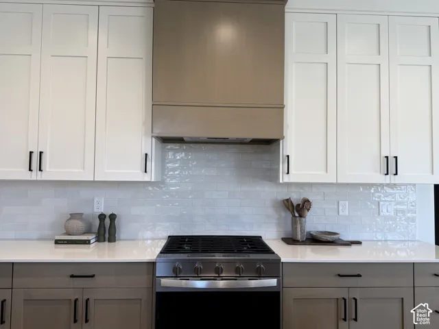 Two-tone cabinetry with contrasting hardware, light subway tile backsplash, stainless steel range, and light-toned countertops