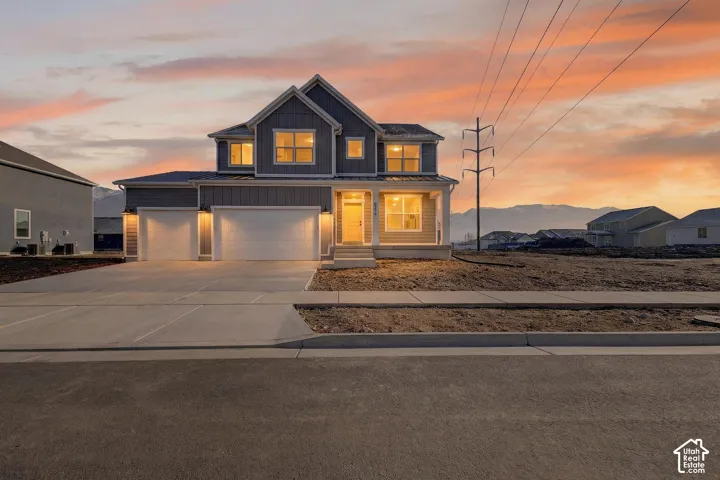 View of front of property with board and batten siding, driveway, covered porch, and an attached garage