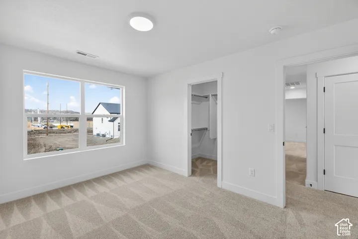 Unfurnished bedroom with light carpet and a spacious closet