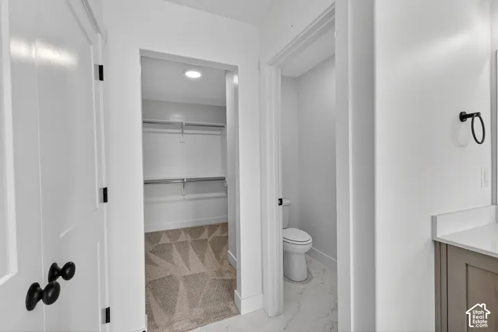 Bathroom featuring light marble finish flooring, a spacious closet, and vanity