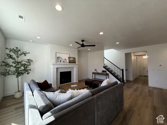 Fireplace with mantel, recessed lighting, wood-finish flooring, ceiling fan, and staircase with metal railing