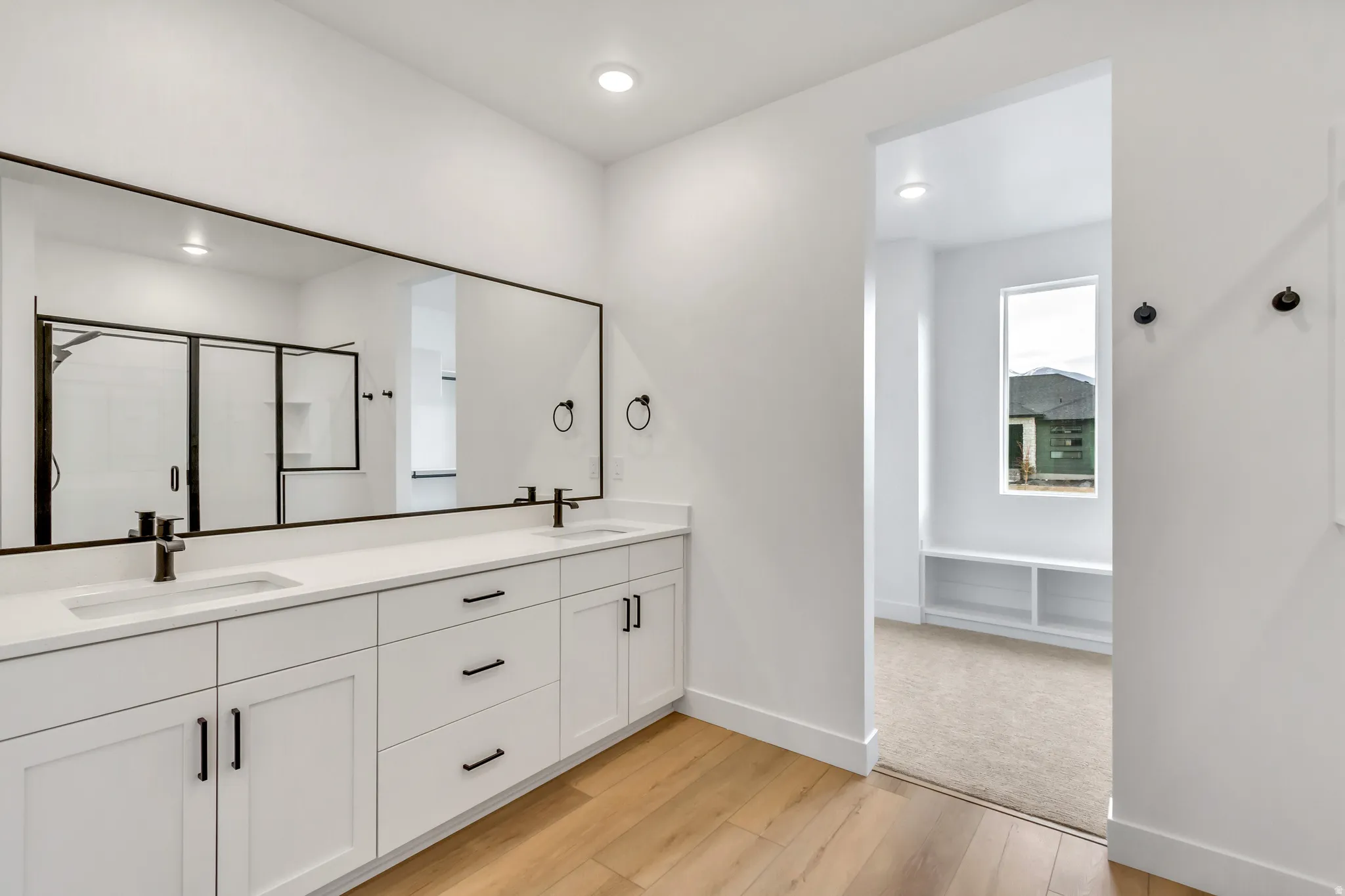 Bathroom with double vanity, a stall shower, light wood-type flooring, and recessed lighting