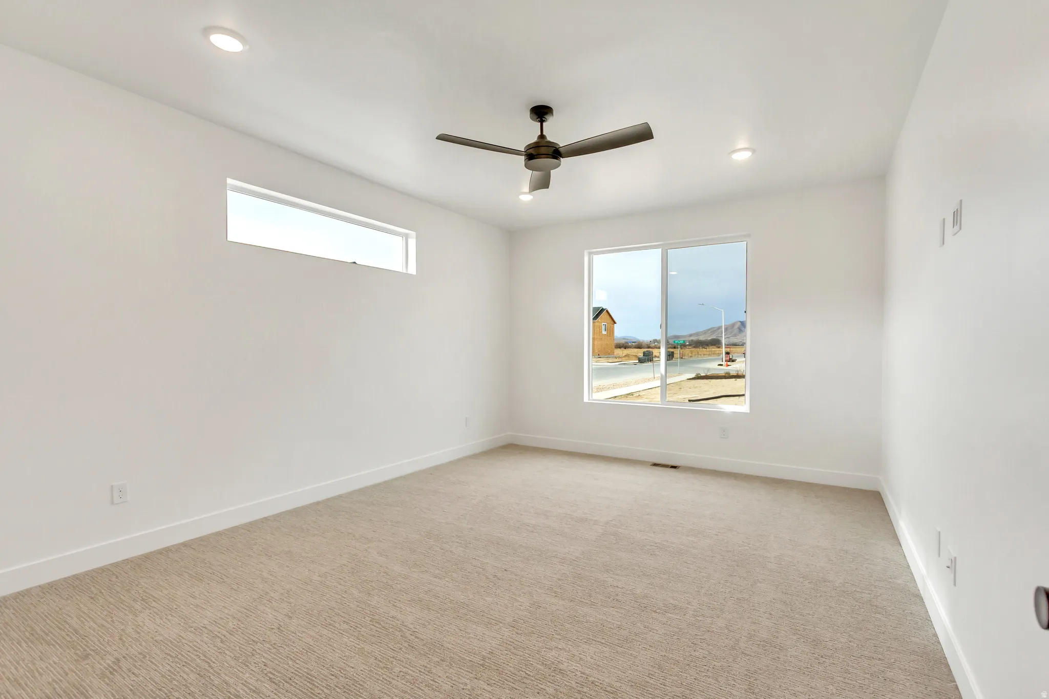 Empty room with light colored carpet, a ceiling fan, plenty of natural light, and recessed lighting