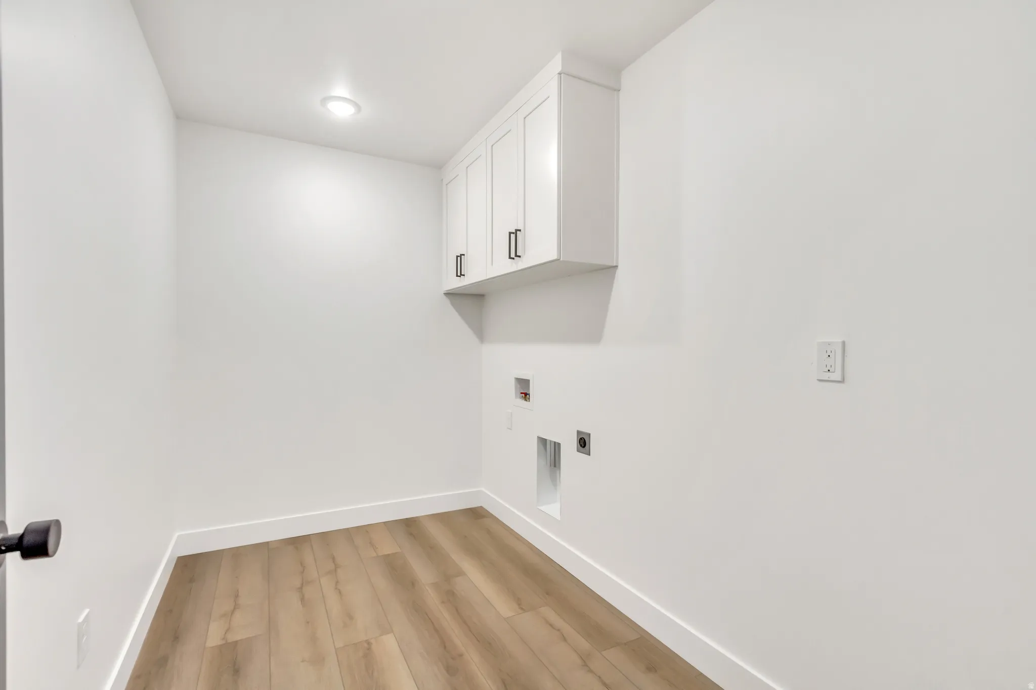 Laundry area featuring light wood-style flooring, washer hookup, and cabinet space