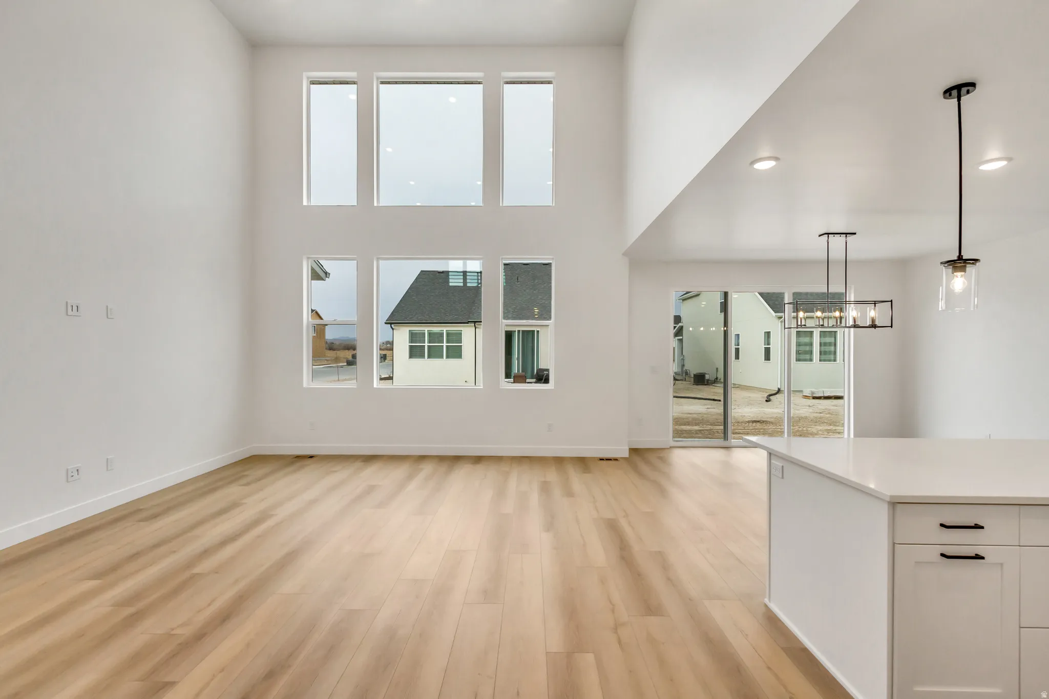 Unfurnished living room featuring light wood-type flooring, a high ceiling, and suspended lighting