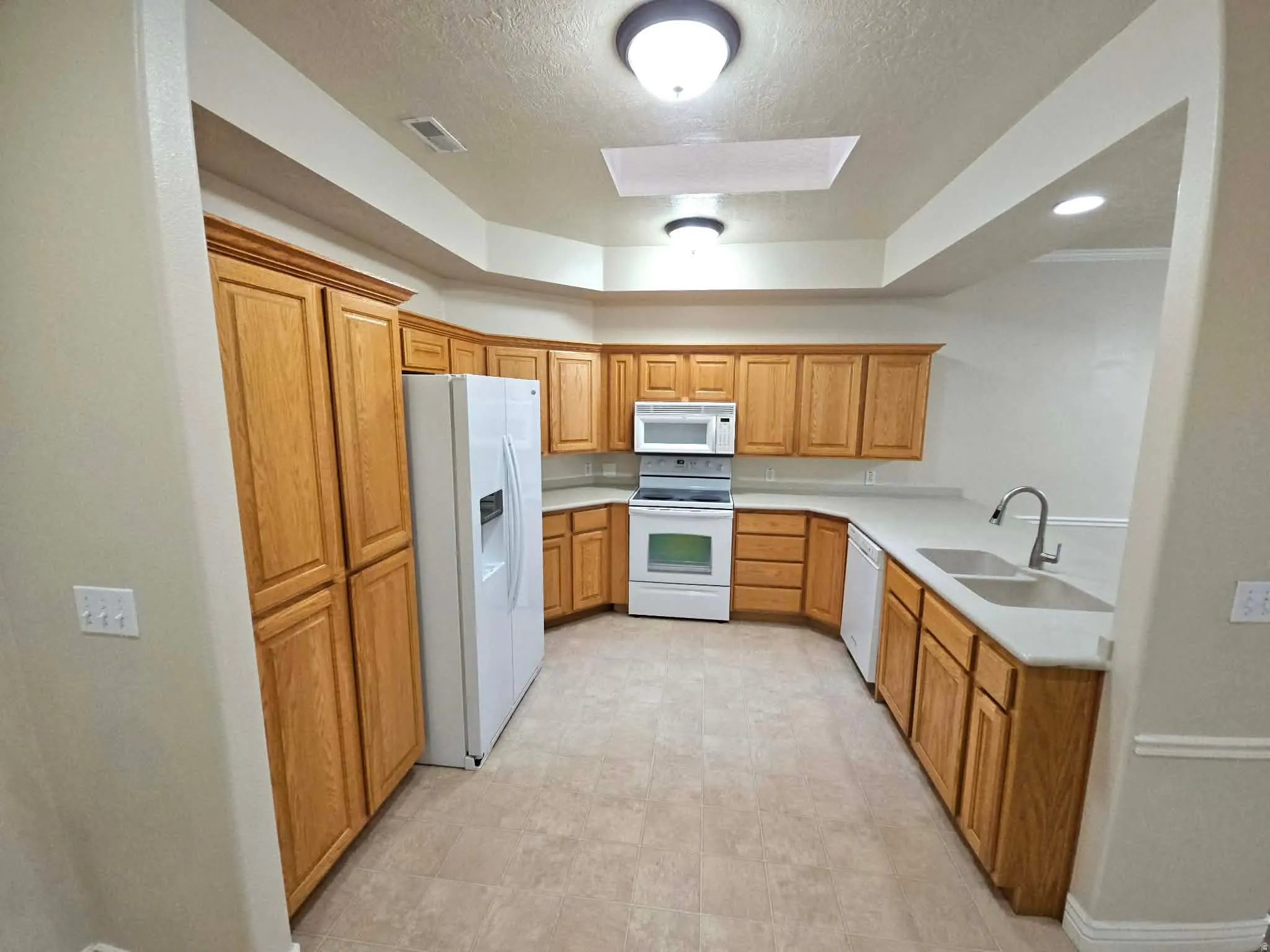 Kitchen with white appliances, wood finish cabinets, and a skylight