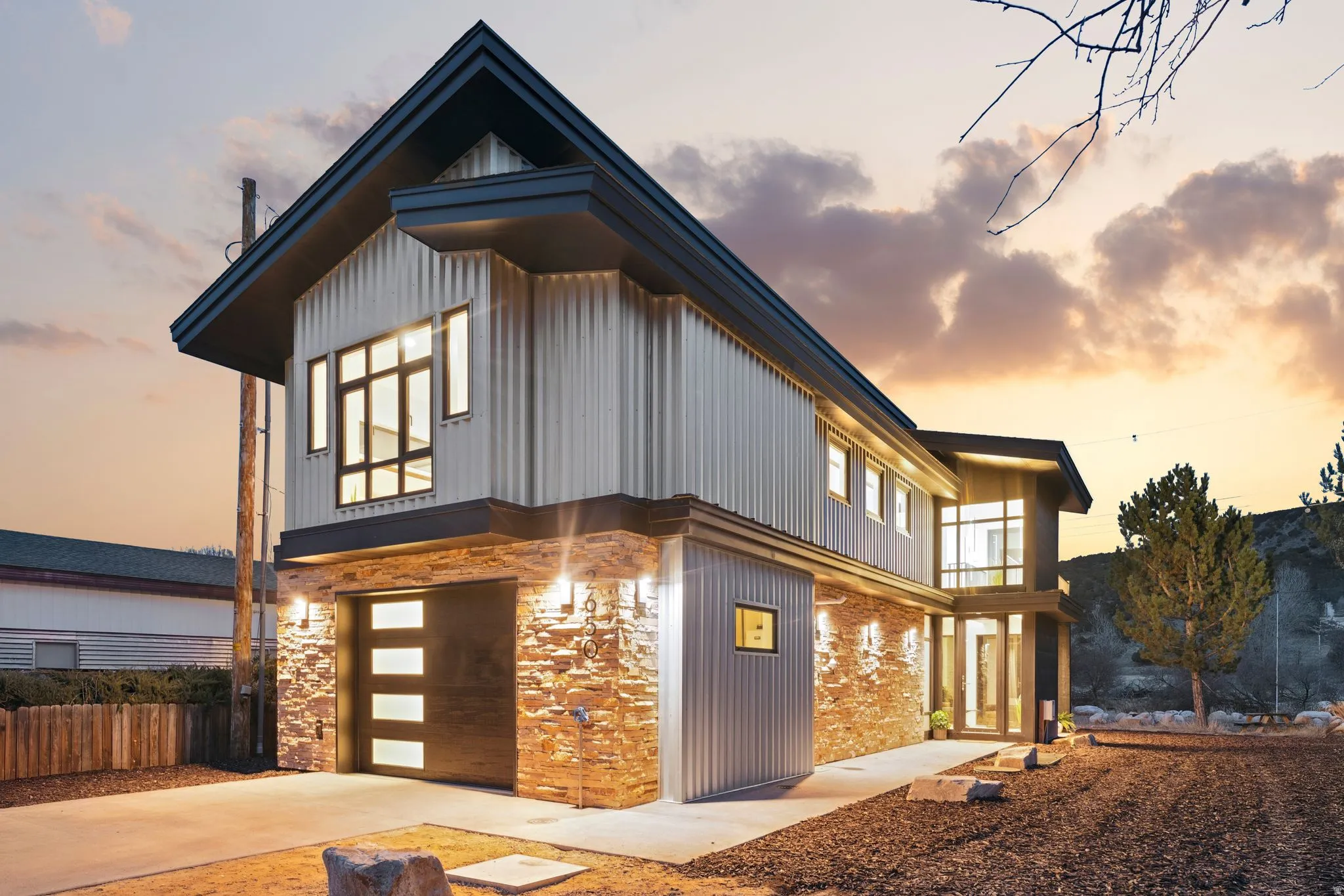 View of front of property featuring a garage, stone siding, driveway, a balcony, and board and batten siding