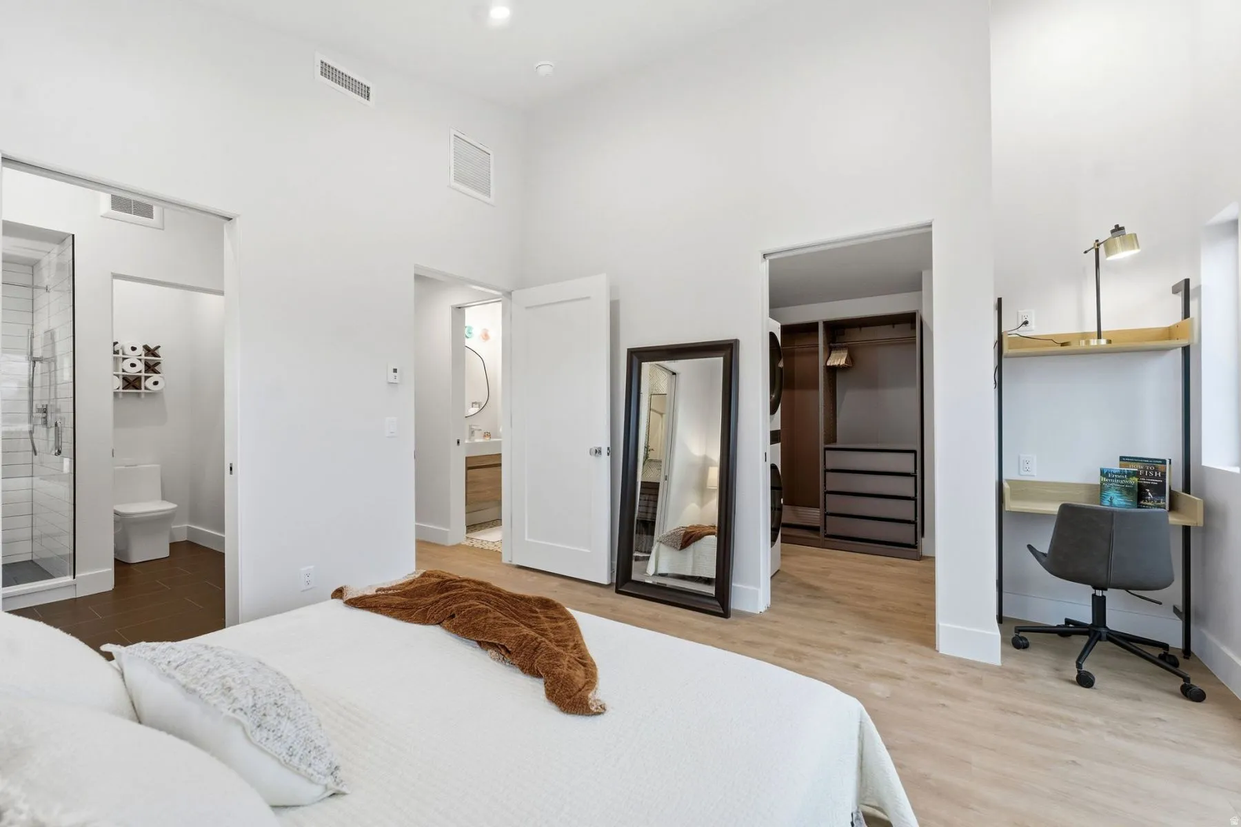 Bedroom with a walk in closet, ensuite bath, light wood-style floors, and a high ceiling