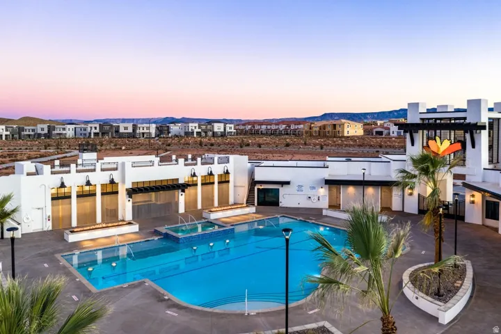 Pool at dusk with a patio area, a pool with connected hot tub, and a pergola