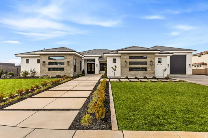 Prairie-style house featuring a front lawn, concrete driveway, stone siding, an attached garage, and stucco siding