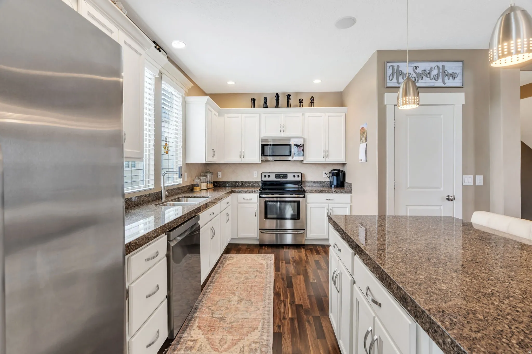 Kitchen featuring stainless steel appliances, white cabinetry, dark wood finished floors, and decorative light fixtures