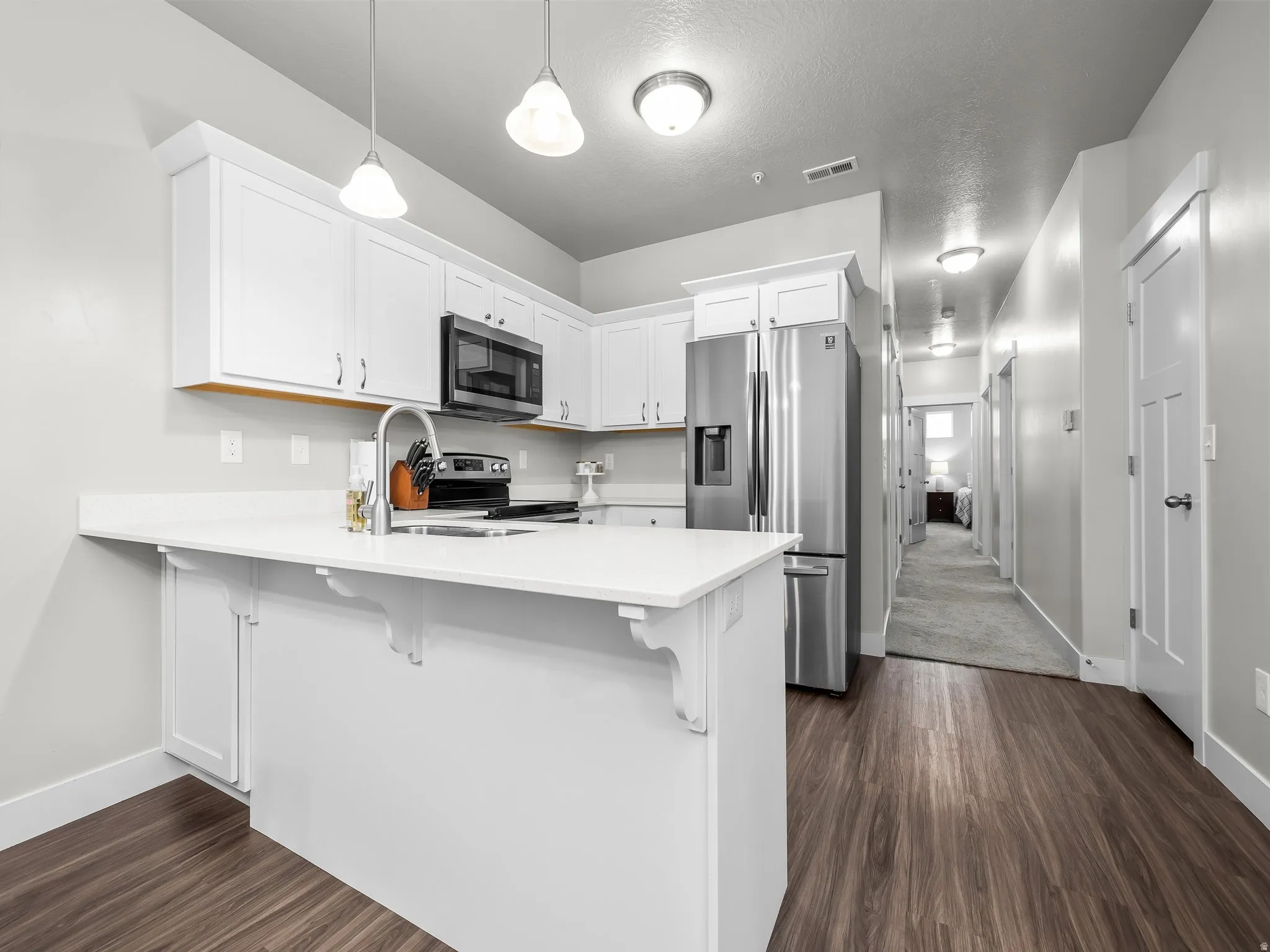 Kitchen with stainless steel appliances,  white cabinets, a peninsula, and pendant lighting