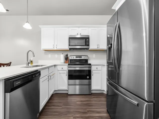 Kitchen with stainless steel appliances, white cabinetry, a peninsula, and decorative light fixtures