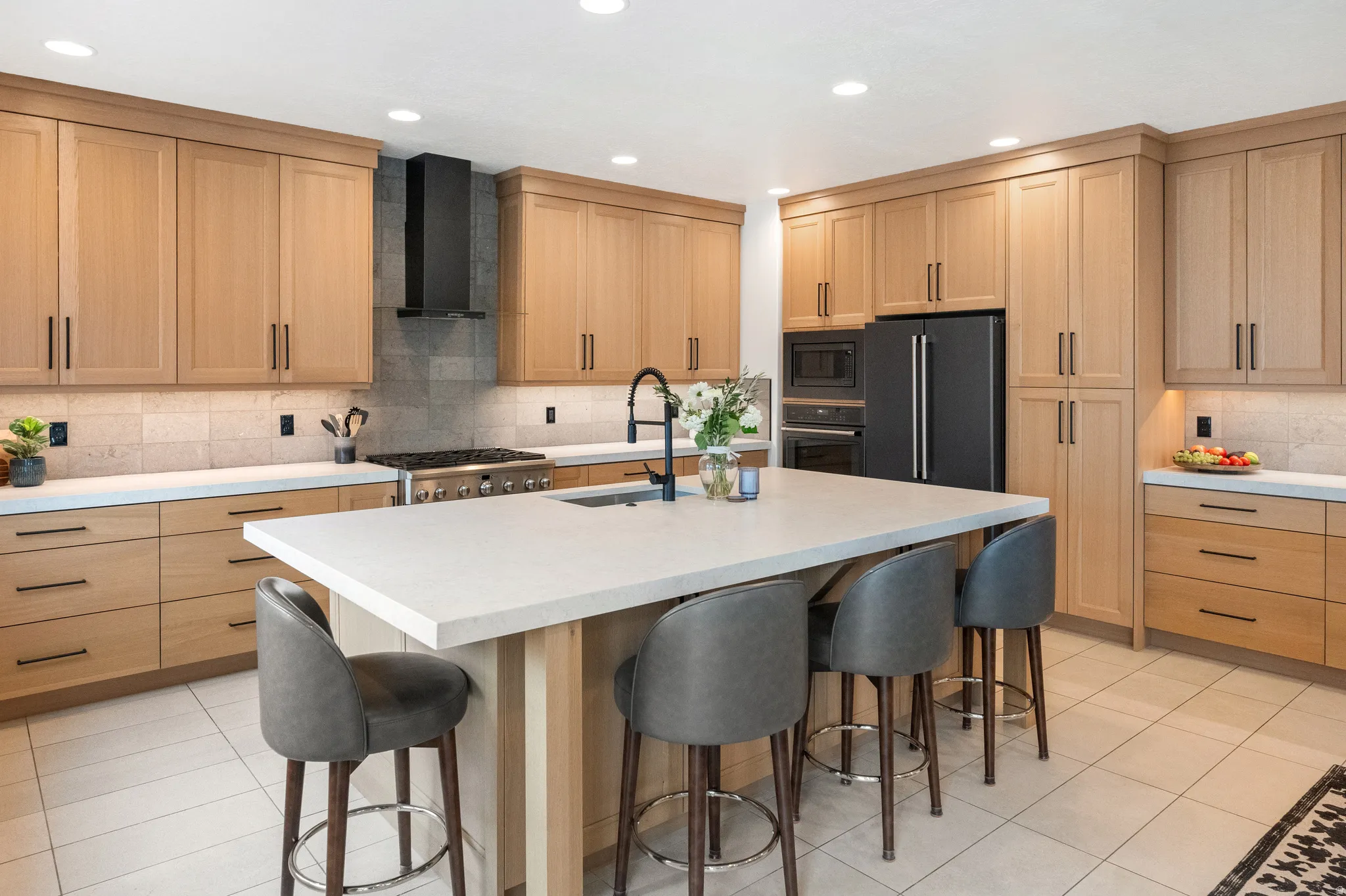 Kitchen featuring white oak cabinetry, decorative backsplash, a kitchen breakfast bar, black appliances, and recessed lighting