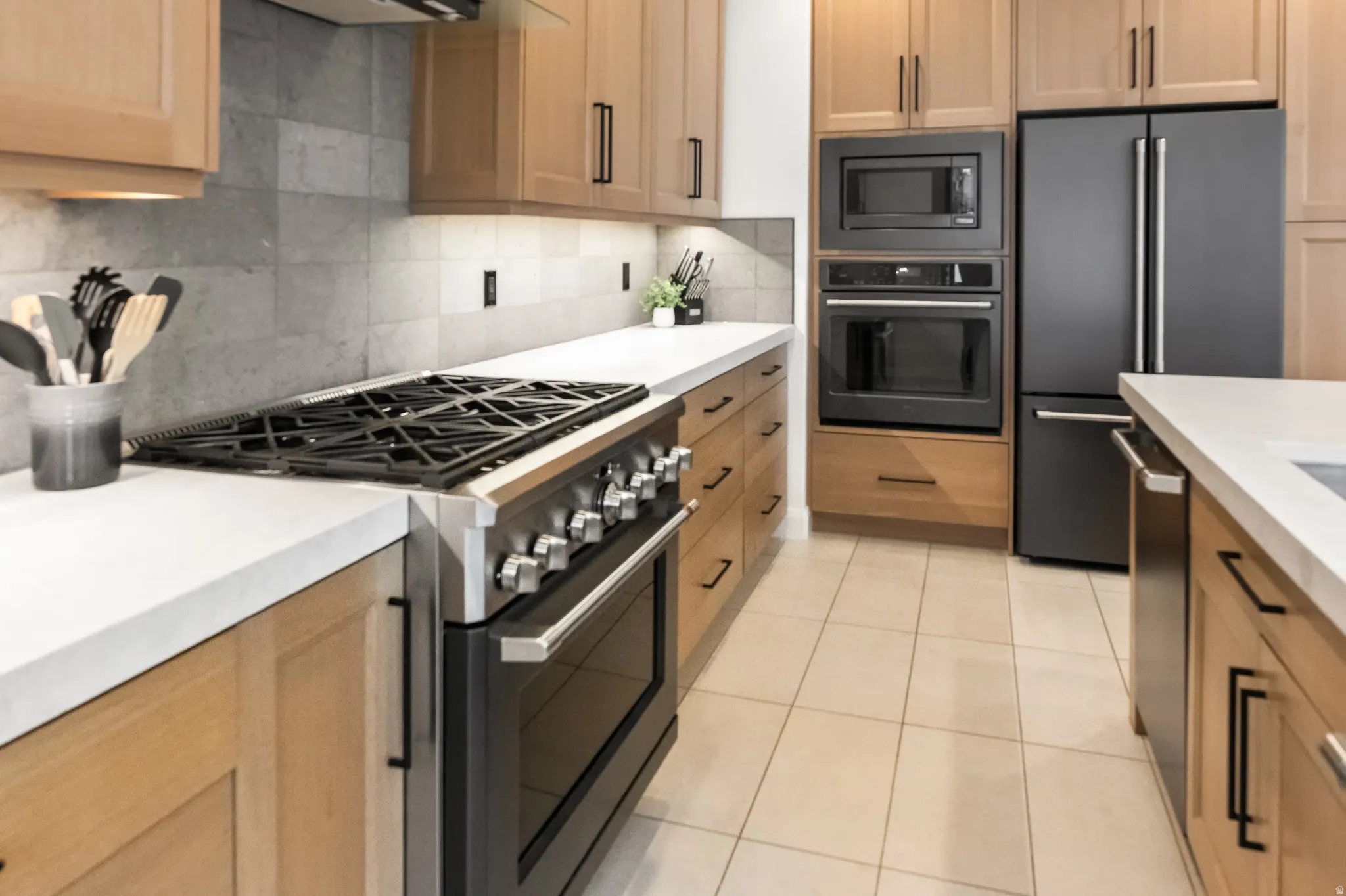 Kitchen with stainless steel appliances, light tile patterned flooring, backsplash, and light stone counters