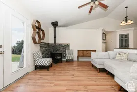 Living area featuring vaulted ceiling, light wood-style floors, a wood stove, ceiling fan, and a chandelier