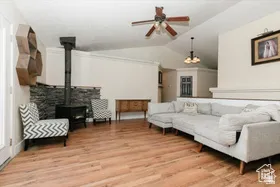 Living area with a wood stove, lofted ceiling, a ceiling fan, and light wood-type flooring