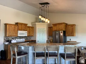 Kitchen featuring a kitchen bar, wood finish cabinets, hanging light fixtures, white appliances, and a textured ceiling