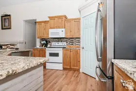 Kitchen with white appliances, light stone counters, light wood-style floors, and backsplash