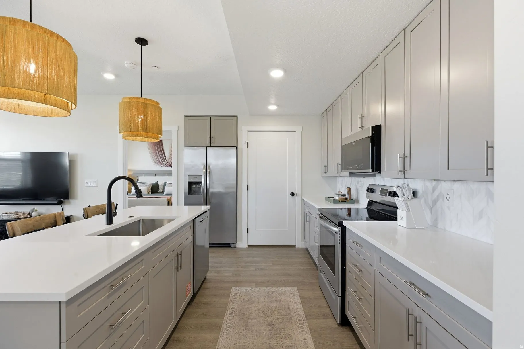 Dual tone kitchen featuring stainless steel appliances, an island with sink, hanging light fixtures, light wood-type flooring, and light stone counters