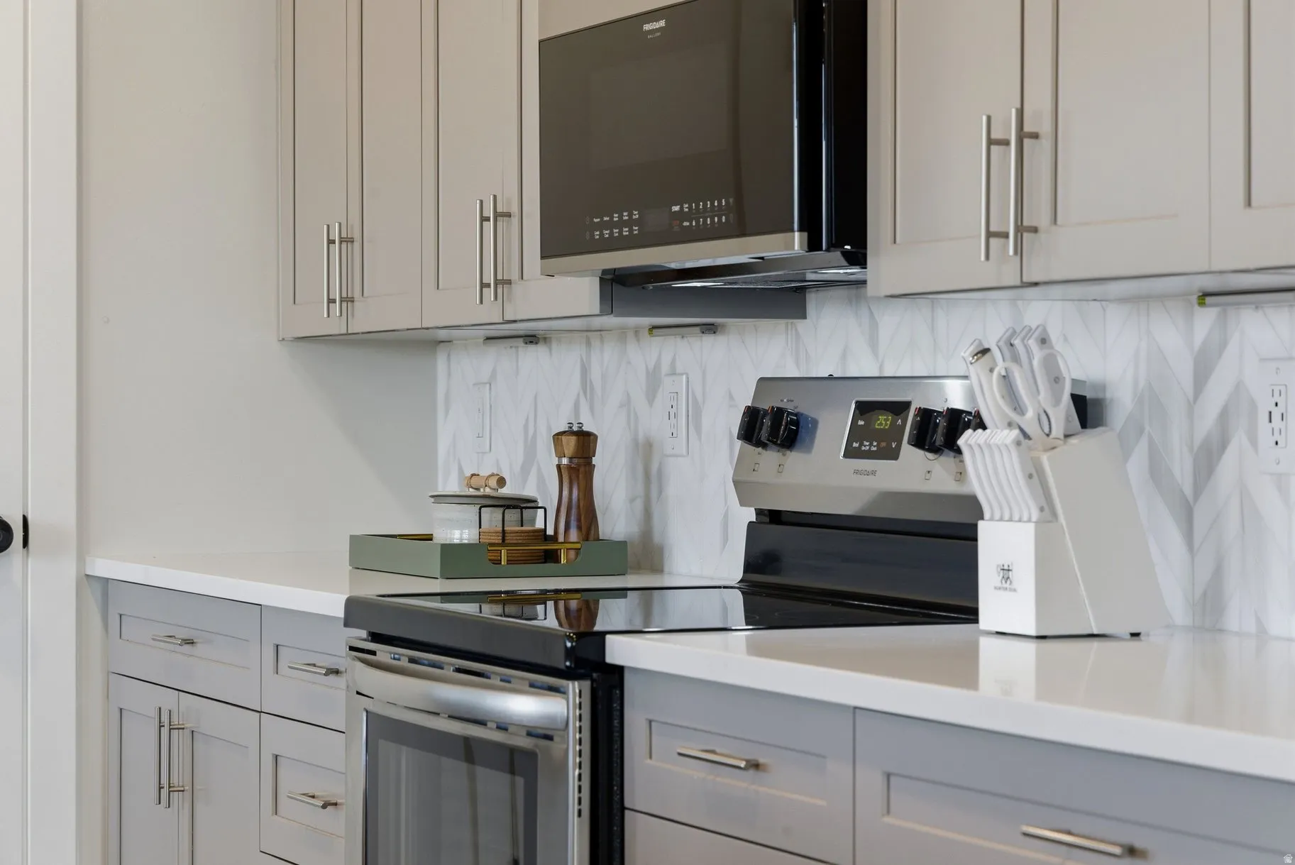 Kitchen featuring stainless steel electric range, gray cabinets, black microwave, and tasteful backsplash