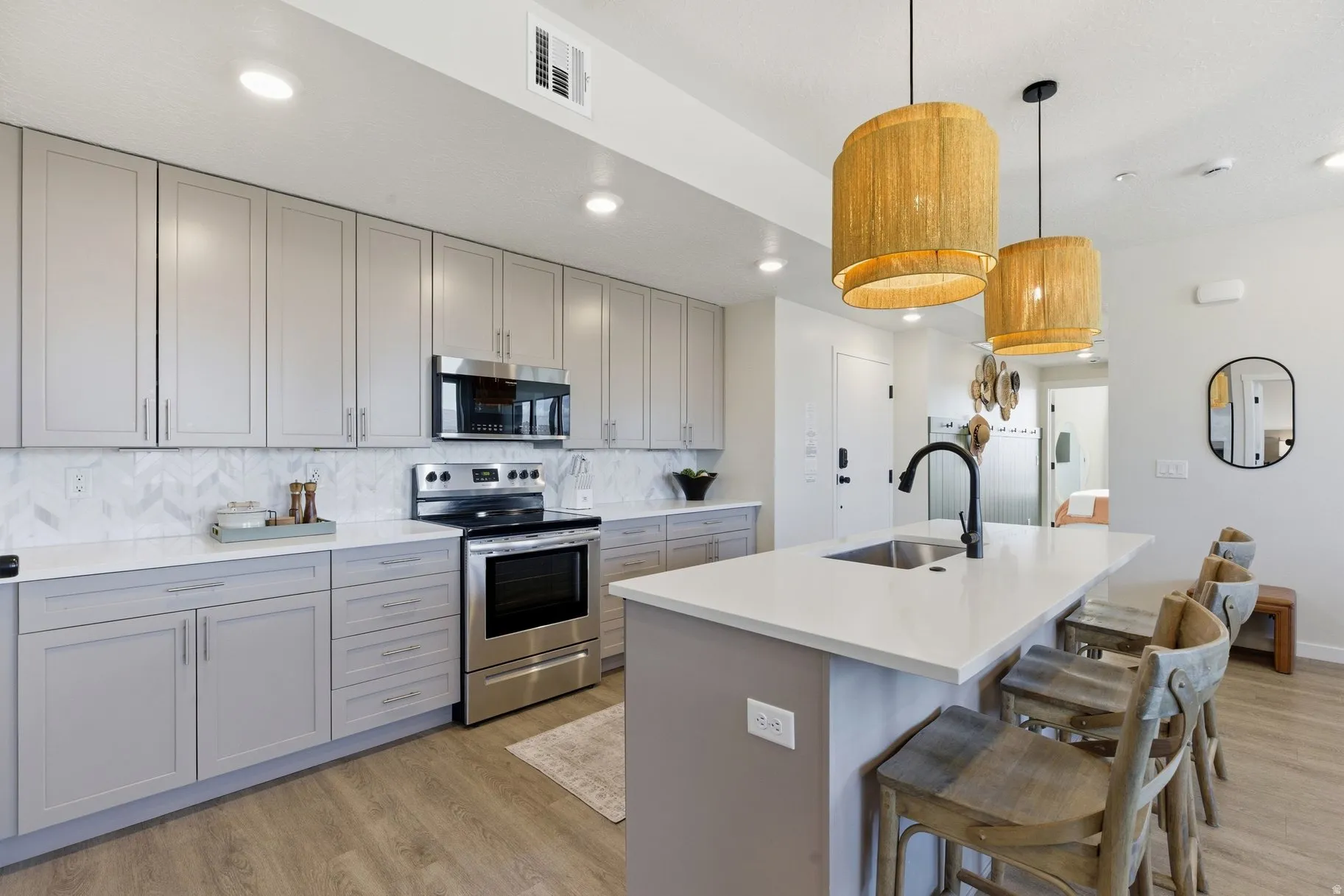 Kitchen with gray cabinets, stainless steel appliances, light wood finished floors, and a center island with sink