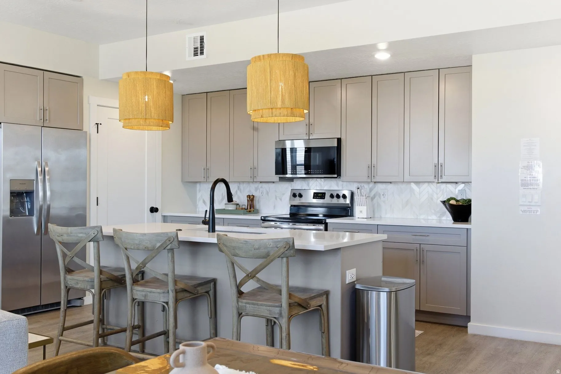 Kitchen with gray cabinets, stainless steel appliances, a kitchen bar, a kitchen island with sink, and light wood-type flooring
