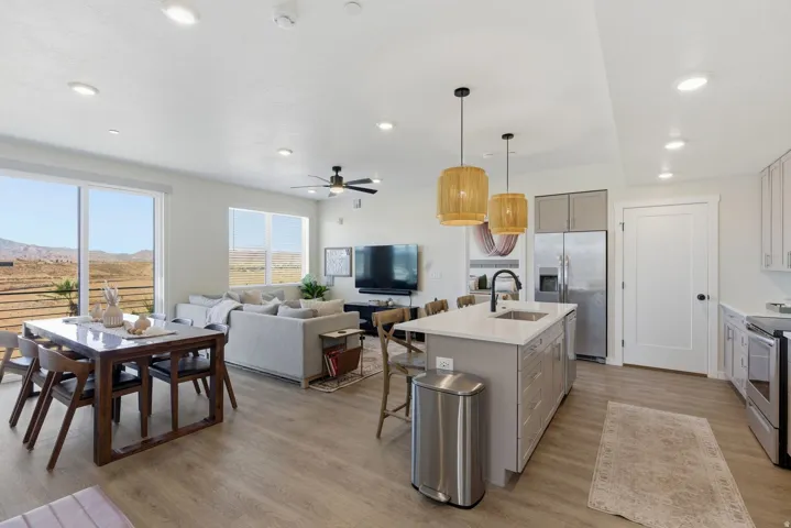Dual tone kitchen with a center island with sink, open floor plan, light wood-style floors, hanging light fixtures, and stainless steel appliances