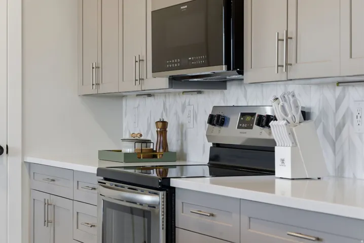 Kitchen featuring stainless steel electric range, gray cabinets, black microwave, and tasteful backsplash