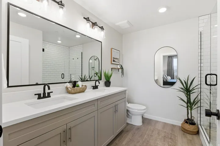 Bathroom with double vanity, a shower stall, light wood-style floors, and recessed lighting