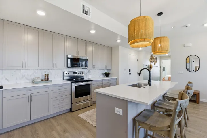 Kitchen with gray cabinets, stainless steel appliances, light wood finished floors, and a center island with sink